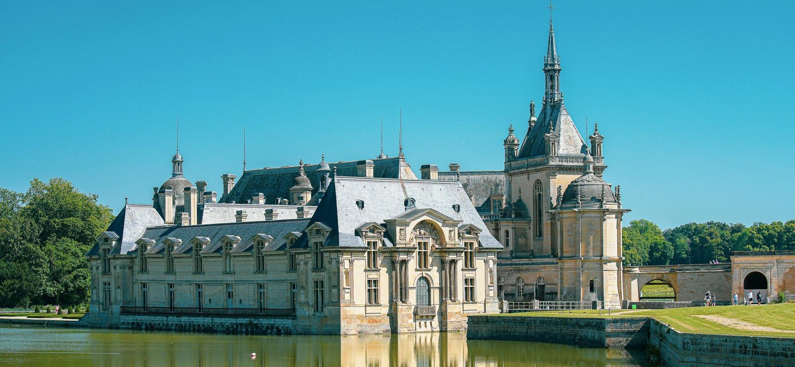 Vue du Château de Chantilly au bord de l’eau, sous un ciel bleu.